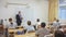 Back view of group of teenage students studying in classroom with male teacher