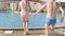 Back view happy boy and girl running and jumping in swimming pool, children having fun, splashing water. Summer travel
