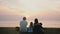 Back view happy family of four sitting together watching the waves at amazing tropical sunset ocean beach with epic sky.