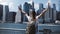 Back view of happy female tourist with backpack raising arms wide open at New York skyline view, looking back at camera.