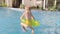 Back view happy girl running and jumping in inflatable swimming ring in swimming pool, children having fun, splashing