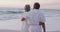 Back view of happy hispanic just married senior couple embracing on beach at sunset