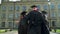 Back view of happy joyful students in black and red mantles celebrating their graduation in front of university building