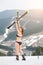 Back view of happy woman skier in swimsuit standing on the slope and holding skis above head