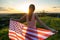 Back view of happy woman with USA national flag standing outdoors at sunset. Positive girl celebrating United States independence