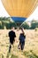 Back view of happy young woman and man in summer field, ready to make balloon tour, standing in front of air balloon