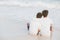 Back view homosexual portrait young asian couple sitting hug together on beach in summer