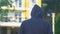 Back view of hooded man walking alone at city street, life problems, loneliness