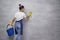 Back view of housewife or maid woman uniform and yellow rubber gloves holding bucket or basket with different cleaning