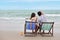 Back view image in love asian couple woman and man who wearing swimming suit sitting and poiting something on deck chair on the