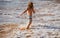 Back view of kid boy have fun on tropical sea beach. Funny child run with splashes by water pool along surf edge. Kids