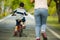 Back view lifestyle portrait of mother and young happy son at city park having fun together the kid learning bike riding and the