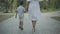 Back view of little boy holding hand of unrecognizable woman as walking along summer alley in park. Relaxed Middle