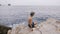 Back view. Little boy in shorts with cap sits on the stony beach in the rocky bay on a sunny day. Small child looks on