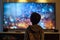 Back view of a little boy sitting in front of tv. Child watching television in dark living room. Films and movies for family.