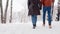 Back view of loving couple feet walking in a park on snowfall. Man and his girlfriend holding hands enjoying snow on