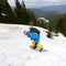 Back view of male backpacker moving down on snowboard. Wooded mountains on background. Off-piste extreme snowboarding