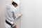 Back view of male drywall worker or plasterer taking measures with meter and pencil, isolated on plasterboard white wall. Wearing