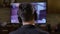 Back view of male gamer guy wearing headphones playing fps action shooter video game on TV console at home -