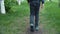 Back view male legs on teenager boy in sneakers walking on grass path on green lawn in summer city. Running male legs in