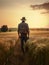 Back view of a male mid-aged farmer standing in the field. Man in jeans, shirt and hat looks at the ripe wheat at sunset.