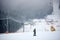 Back view of male skier standing on middle of slope and admiring foggy wooded mountains view. Equipped ski run at resort