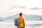 Back view of male tourist with rucksack standing on coast in front of great mountain while journey