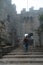 Back view Man with backpack walking alone goes up the stairs. Fortification, old castle. Journey. Mystical atmosphere, fog, white