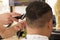 Back view of man getting short hair trimming at barber shop with clipper machine