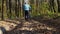 Back view. A man is rolling his bicycle along a forest road studded with foliage. The warm autumn sun is shining on the