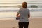 back view of mature woman with sports mat and preparing to practice yoga outdoors on sea beach. overweight woman