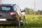 Back view of modern new shiny empty black car parked outside road in grassy looming field on bright summer sunny day on blurred