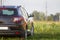 Back view of modern new shiny empty black car parked outside road in grassy looming field on bright summer sunny day on blurred g
