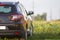 Back view of modern new shiny empty black car parked outside road in grassy looming field on bright summer sunny day on blurred g