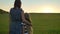 Back view of mother coming and hugging her little blonde daughter, standing in the middle of wheat or rye field