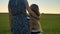 Back view of mother hugging little daughter with long blonde hair, standing in the middle of wheat field and watching