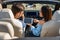 Back view of multiethnic couple using digital tablet for navigating in convertible