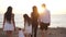 Back view of multigenerational family walking in slow motion to sunset on Mediterranean sea. Carefree happy Caucasian