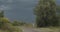 Back view of old country woman walking alone on local road to dark stormy landscape. Unrecognizable elderly lady