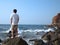 Back view of pensive lonely young Asian man standing on the rock of seashore.