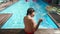 Back view of playful Caucasian boy having fun dancing sitting on poolside in sunshine. Carefree hyperactive kid enjoying