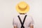 Back view portrait of woman in hat and earrings, wearing white T-shirt and overalls, standing calm unrecognizable studio shot