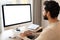 Back view of positive Hindi man in smart casual clothes using computer while sitting at the desk in his flat. Young