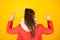 Back view of positive lucky girl raising hands up isolated on yellow background. Woman in casual wear with red nails.