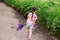 Back view. a preschool girl in shorts and a T-shirt walks along the road alone and carries a bouquet of purple lupins