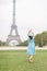 Back view of pretty lady in blue dress and hat, enjoying walk in Paris, near Eiffel tower. Young attractive happy woman