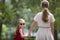 Back view of pretty small blond long-haired child girl in sunglasses and fashionable red dress holding trustingly hand of young