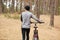 Back view of professional cyclist choosing path in forest, looking aside, holding sport bicycle, united with nature, being fond of