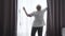 Back view of professional hotel maid opening curtains in hotel room. Diligent Caucasian adult woman preparing