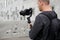 Back view of professional videographer holding dslr camera on 3-axis gimbal over grey concrete building